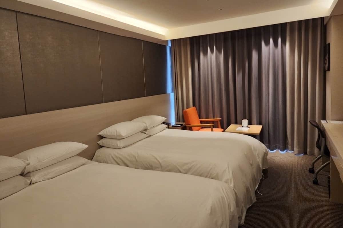 Une chambre d’hôtel avec deux lits, un bureau, une chaise et une grande fenêtre avec des rideaux.