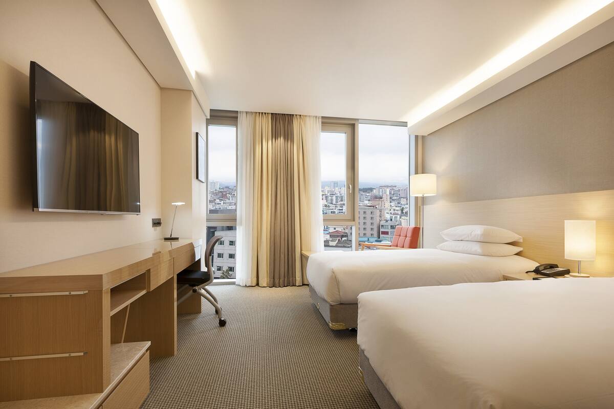 Une chambre d’hôtel avec deux lits, un bureau, une chaise, une télévision et une vue sur la ville.