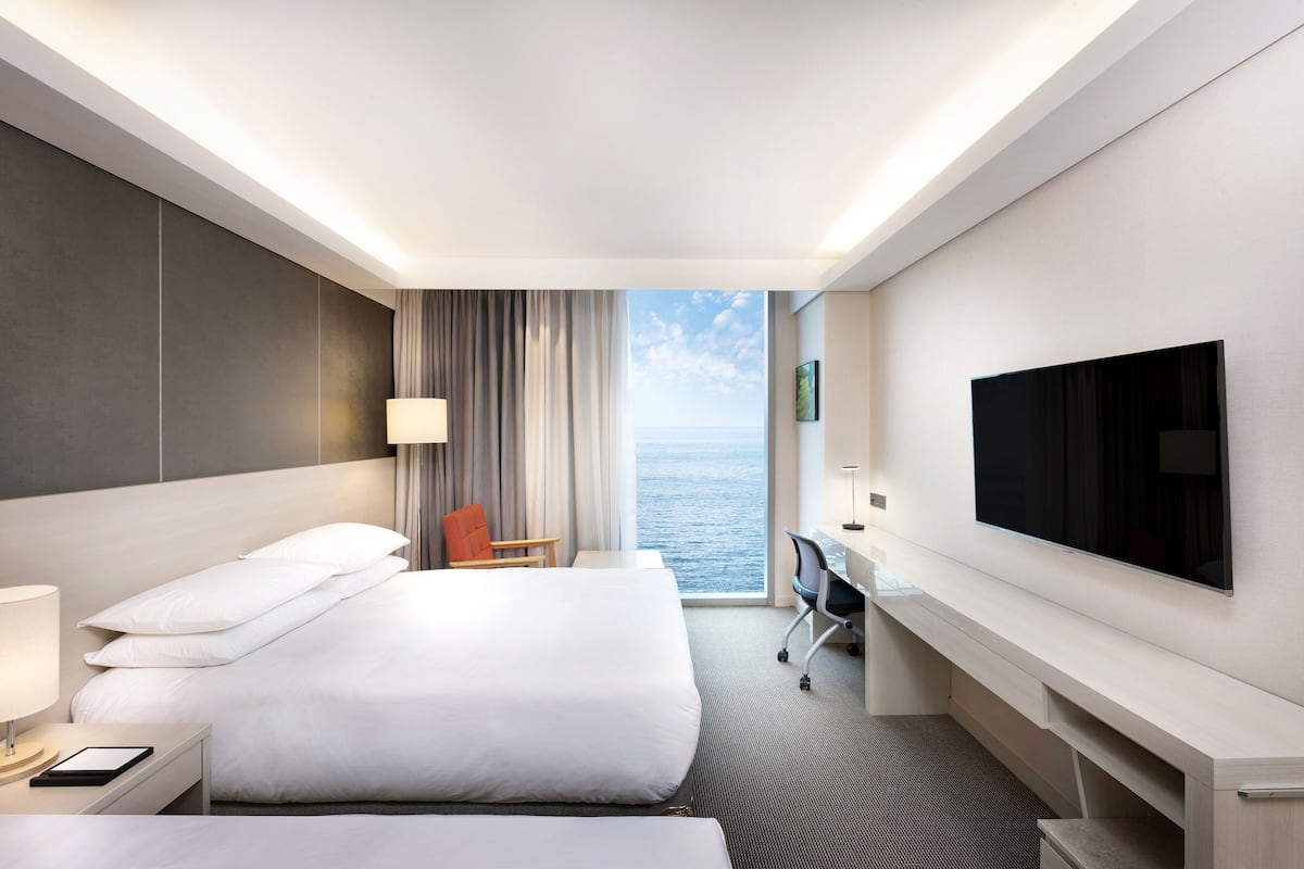 Une chambre d’hôtel avec deux lits, un bureau, une télévision et vue sur la mer.