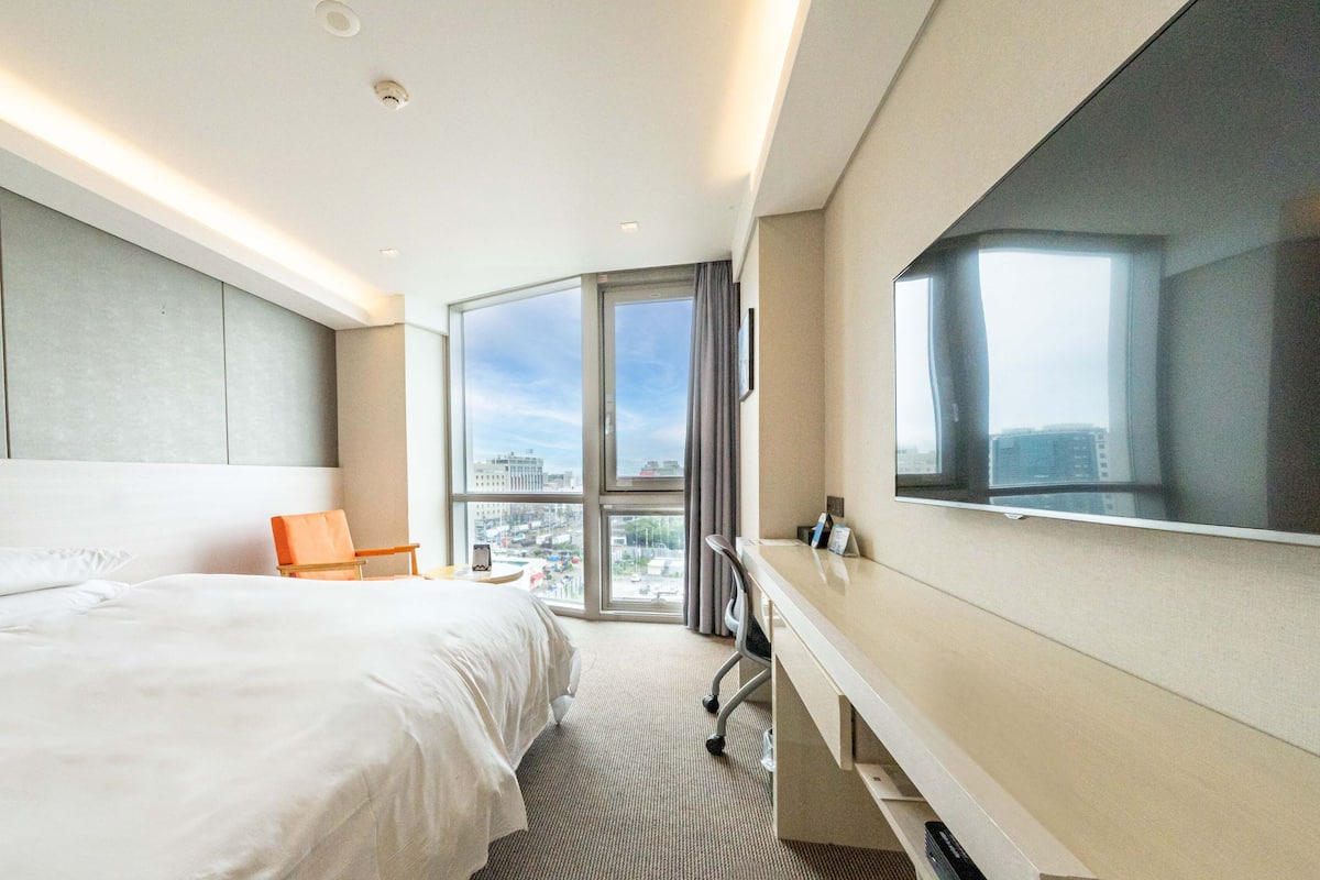 Une chambre d’hôtel moderne dotée d’un grand lit, d’un bureau et d’une grande fenêtre donnant sur la ville.