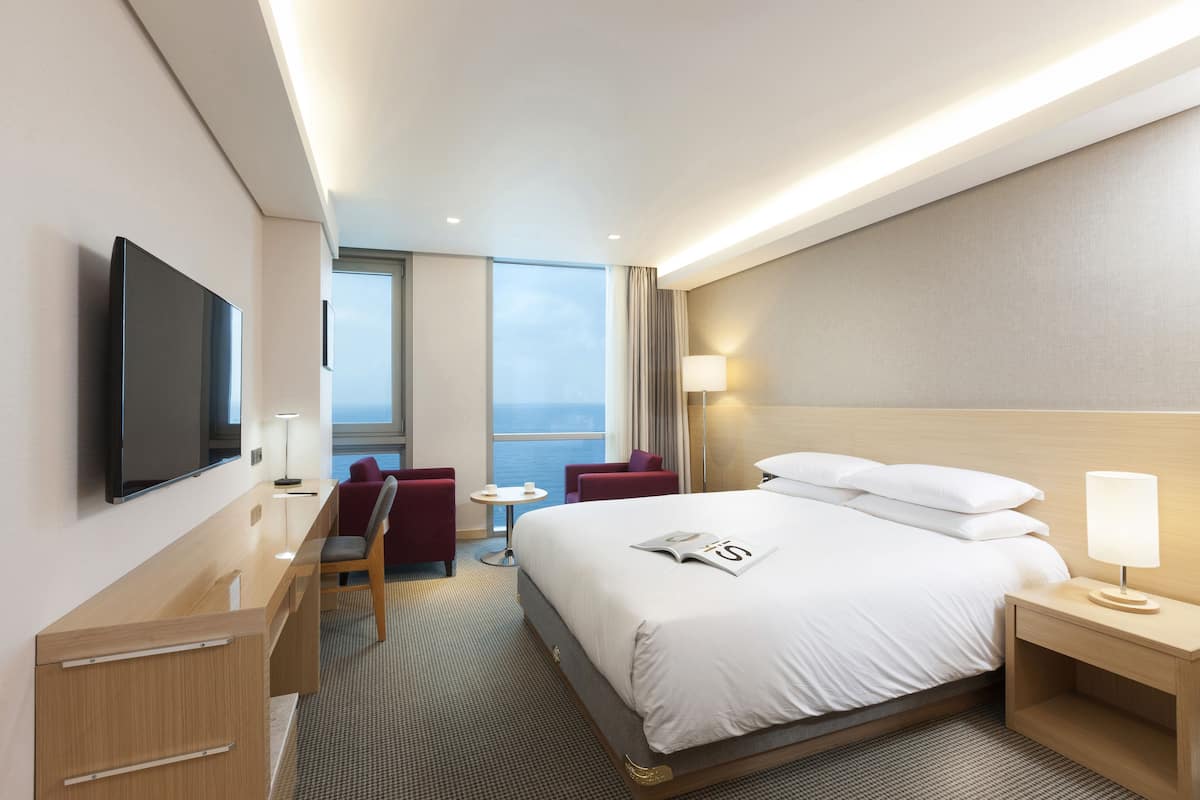 Une chambre d’hôtel moderne dotée d’un grand lit, d’un bureau, d’une chaise, d’une télévision et offrant une vue sur la mer.