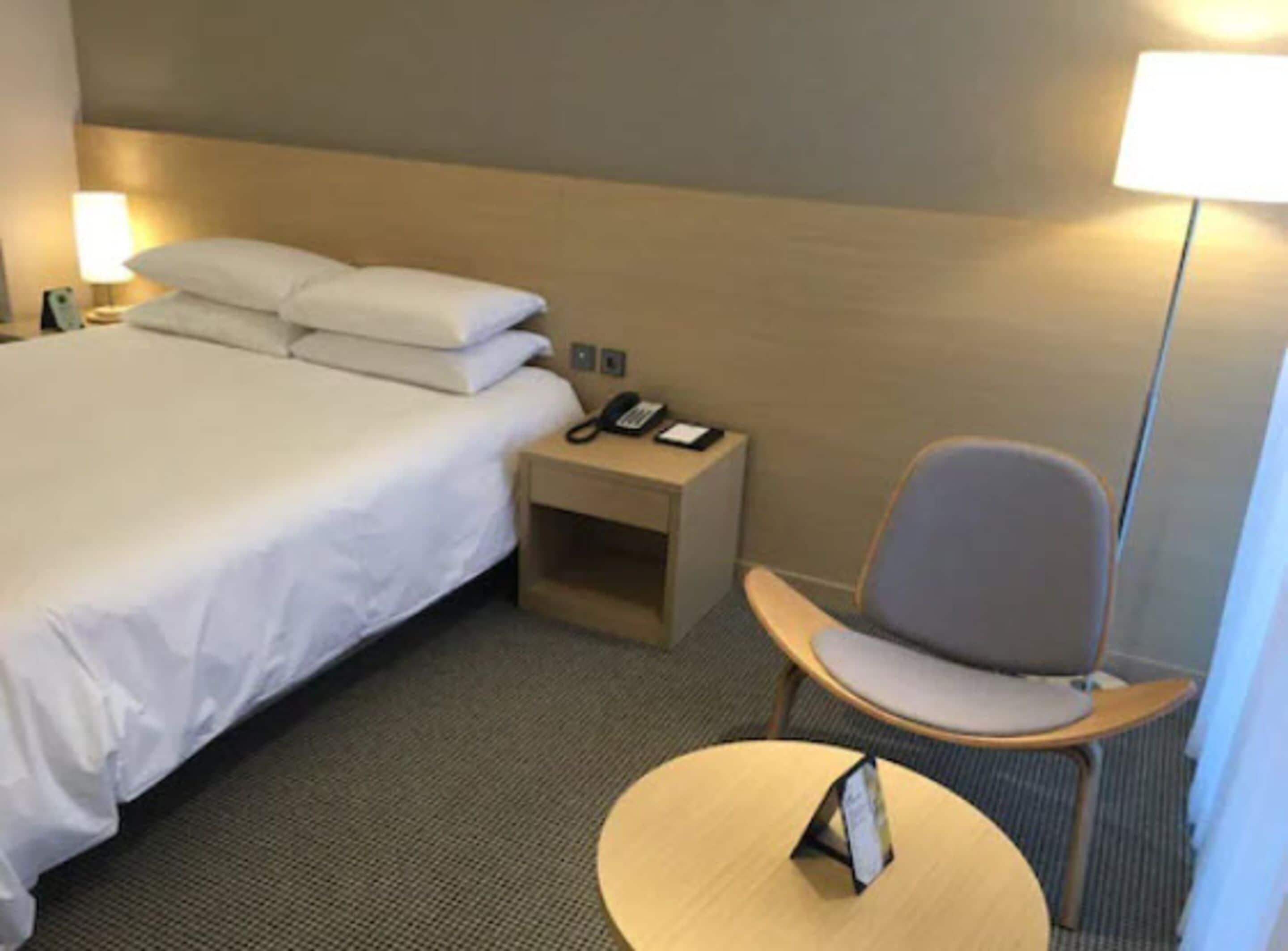 Una habitación de hotel con una cama, una mesita de noche con un teléfono, una silla y una pequeña mesa con un marco de fotos.