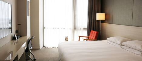 A hotel room with a large bed, a desk, a chair, and a window with curtains.