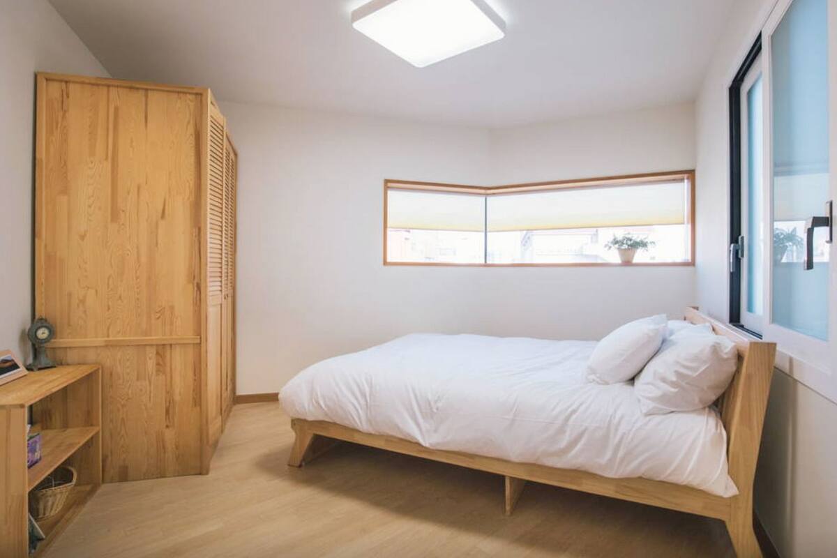 A bedroom with a wooden bed, a wardrobe, a small table, and a window with a view.