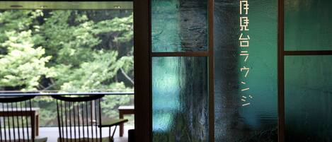 A view through a glass door with a wooden frame, leading to an outdoor area with chairs and a table.