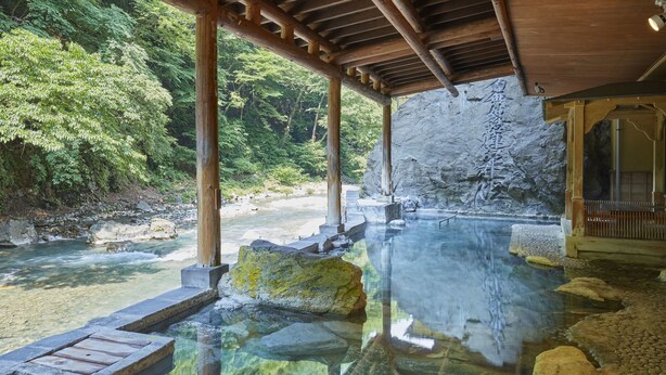 Un onsen japonés tradicional con estructura de madera, agua cristalina y entorno natural.