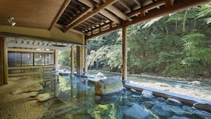 Un onsen japonés tradicional con agua termal cristalina, vigas de madera y vistas a un bosque en la ladera.
