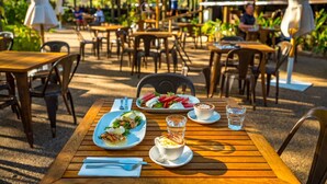 An outdoor dining area with wooden tables and chairs, umbrellas, and a view of the surrounding greenery. - El Questro - Emma Gorge (Durack)