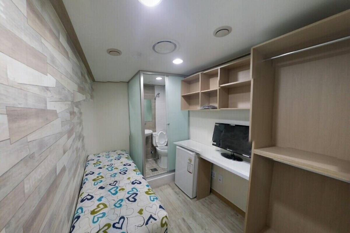 A compact room with a bed, a small desk with a computer, a television, and a wardrobe.