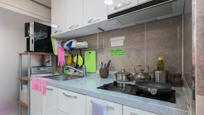 A kitchen with white cabinets, a countertop, a stove, a kettle, and a green cutting board. - Don Quixote Stay (Seoul)