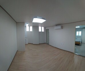 A spacious room with a wooden floor, a large mirror, and a ceiling light.