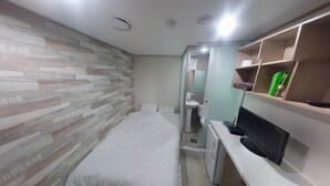 A compact hotel room with a bed, a small desk with a TV, a vanity with a mirror, and a shelf with toiletries. - Don Quixote Stay (Seoul)