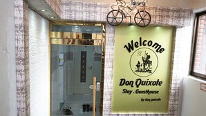 A hotel entrance with a glass door, a bicycle hanging above, and a welcome sign. - Don Quixote Stay (Seoul)
