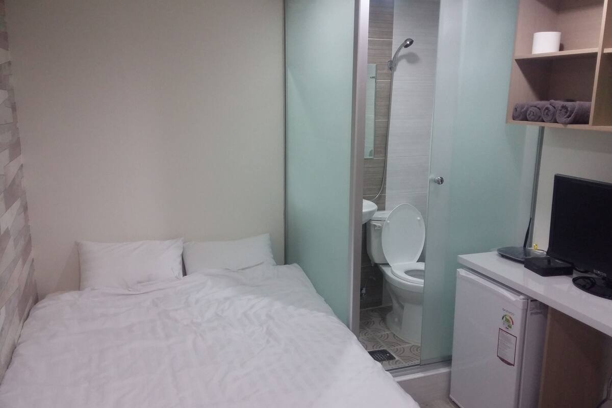 A hotel room with a bed, a toilet, a shower, and a small desk with a computer.