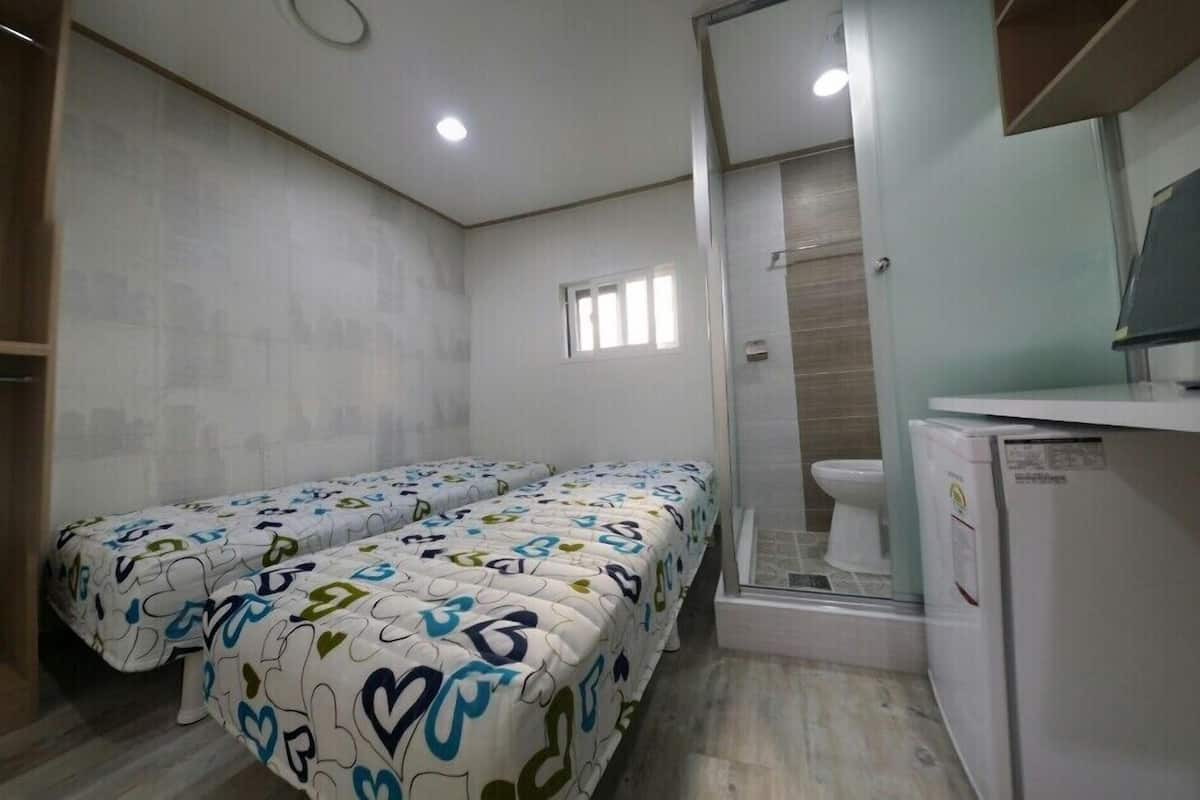 A hotel room with two beds, a shower, a toilet, and a small refrigerator.