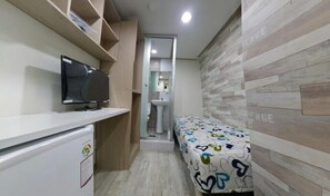 A compact hotel room with a television on a white cabinet, a small bed with a colorful bedspread, and a wooden wall.