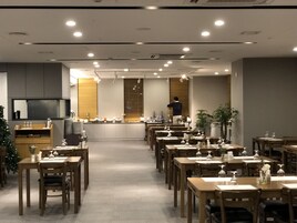 A restaurant with a long counter, wooden tables, and chairs arranged for dining.