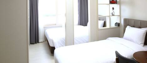A hotel room with two beds, a small table, and a shelf with decorative items.