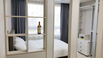 Habitación de hotel con cama, armario, minibar y una botella de whisky Ballantine's en una estantería.