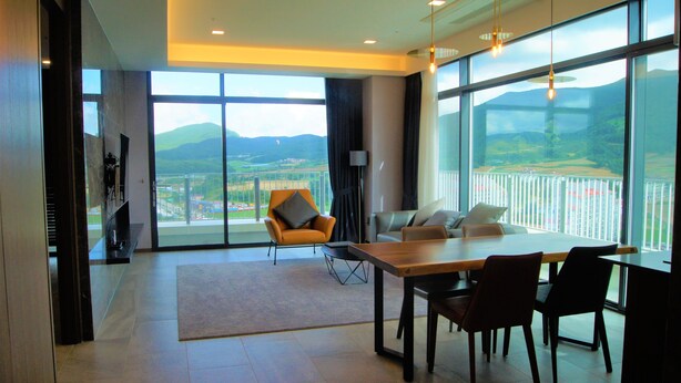 A spacious living area with a large dining table, comfortable seating, and expansive windows offering a view of the countryside. - Am Hotel (Pyeongchang)