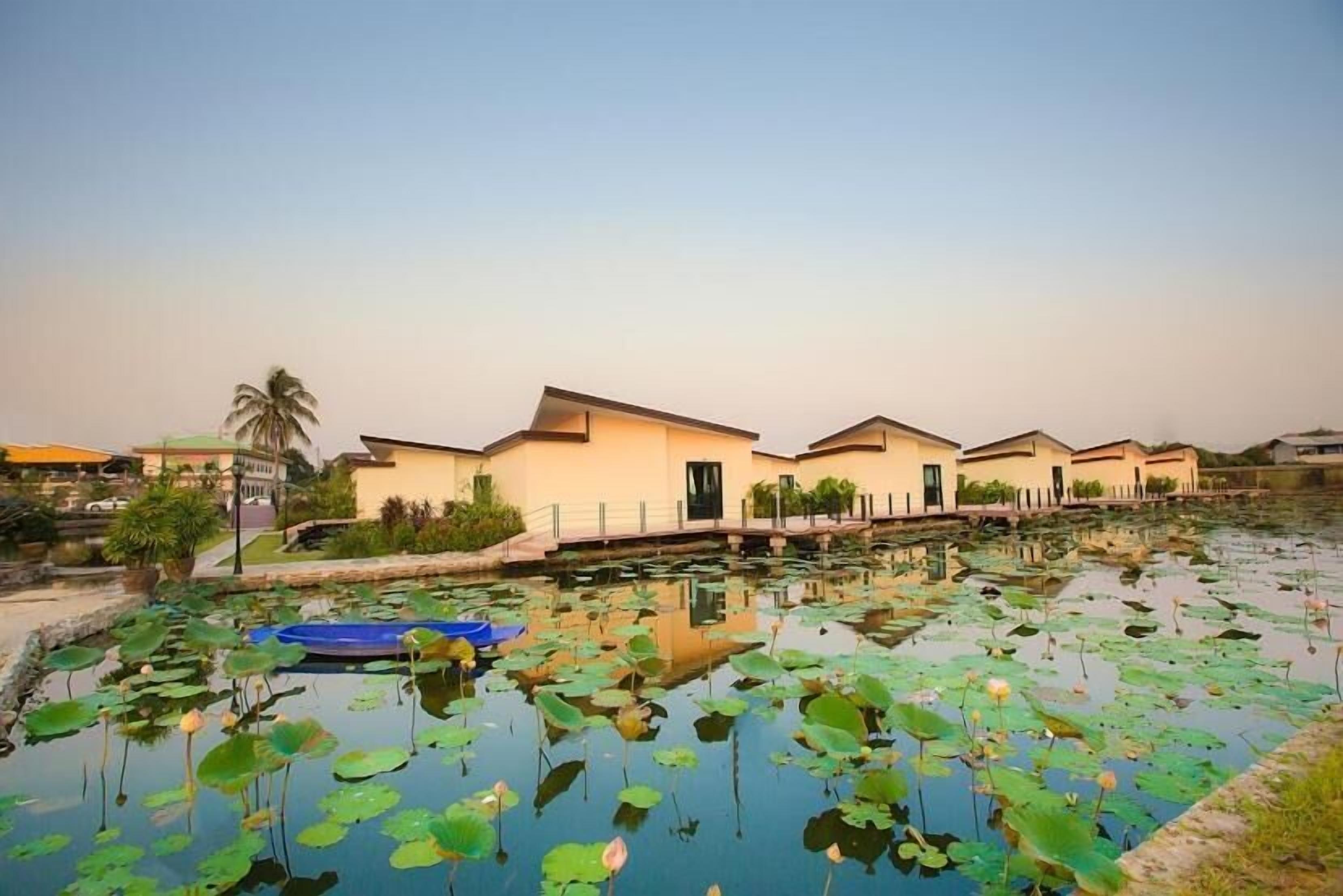 A series of modern buildings with a water body in the foreground, surrounded by greenery.