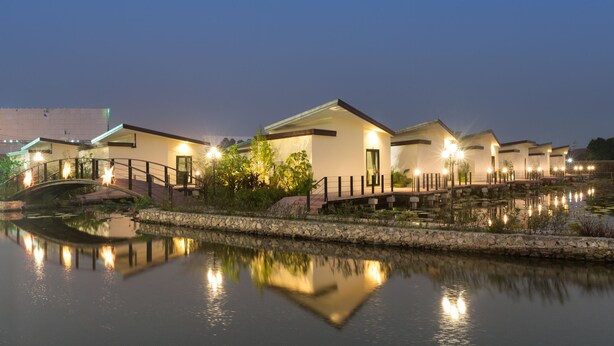 A row of modern, well-lit buildings with a calm water body in the foreground, reflecting the structures. - Bua Tara Resort (Pattaya)
