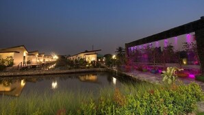 A nighttime view of a resort with a pool, illuminated buildings, and a landscaped area with plants. - Bua Tara Resort (Pattaya)