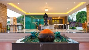 A modern hotel lobby with a central water feature, seating areas, and a reception desk. - Bua Tara Resort (Pattaya)