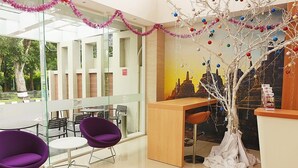 Een moderne receptie met een houten toonbank, paarse stoelen en een decoratieve boom.