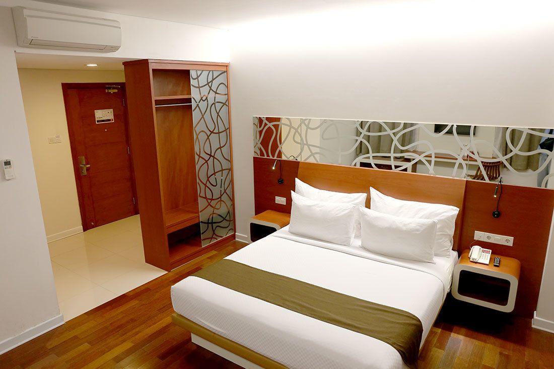 A hotel room with a bed, a wardrobe, a bedside table, and a wall with a geometric pattern.