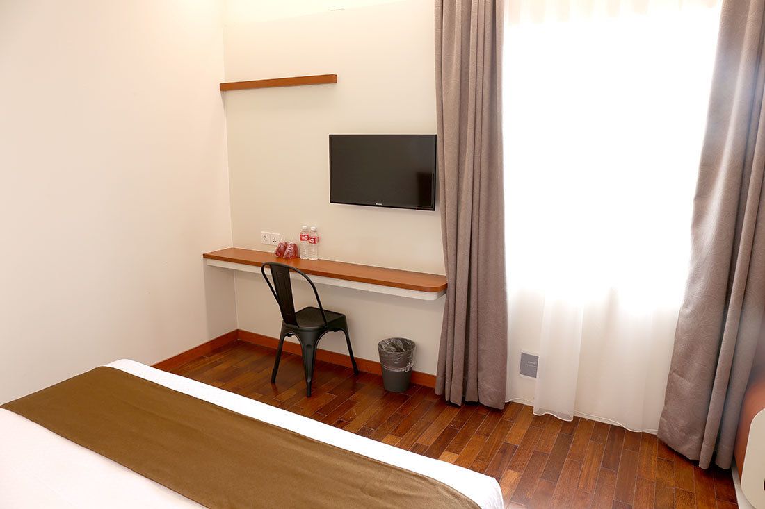 Hotellihuone, jossa on sänky, työpöytä tuolilla, televisio ja ikkuna, jossa on verhot.