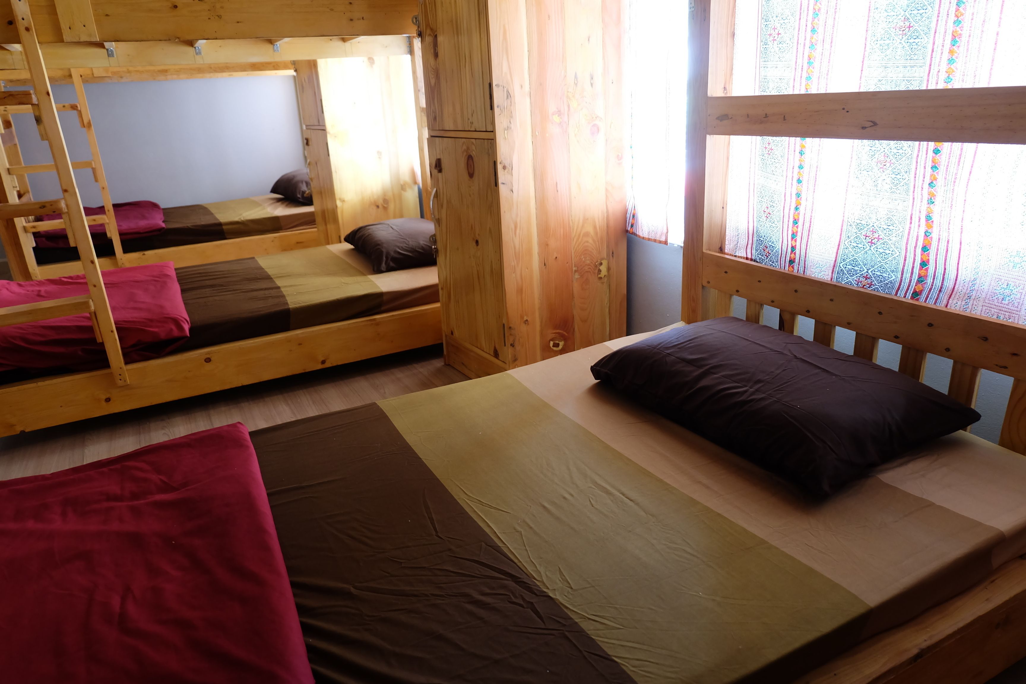 Une cabine avec des lits superposés, des murs en bois et une fenêtre ornée de rideaux à motifs.