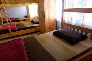 Una cabana amb lliteres, parets de fusta i una finestra amb cortines estampades.