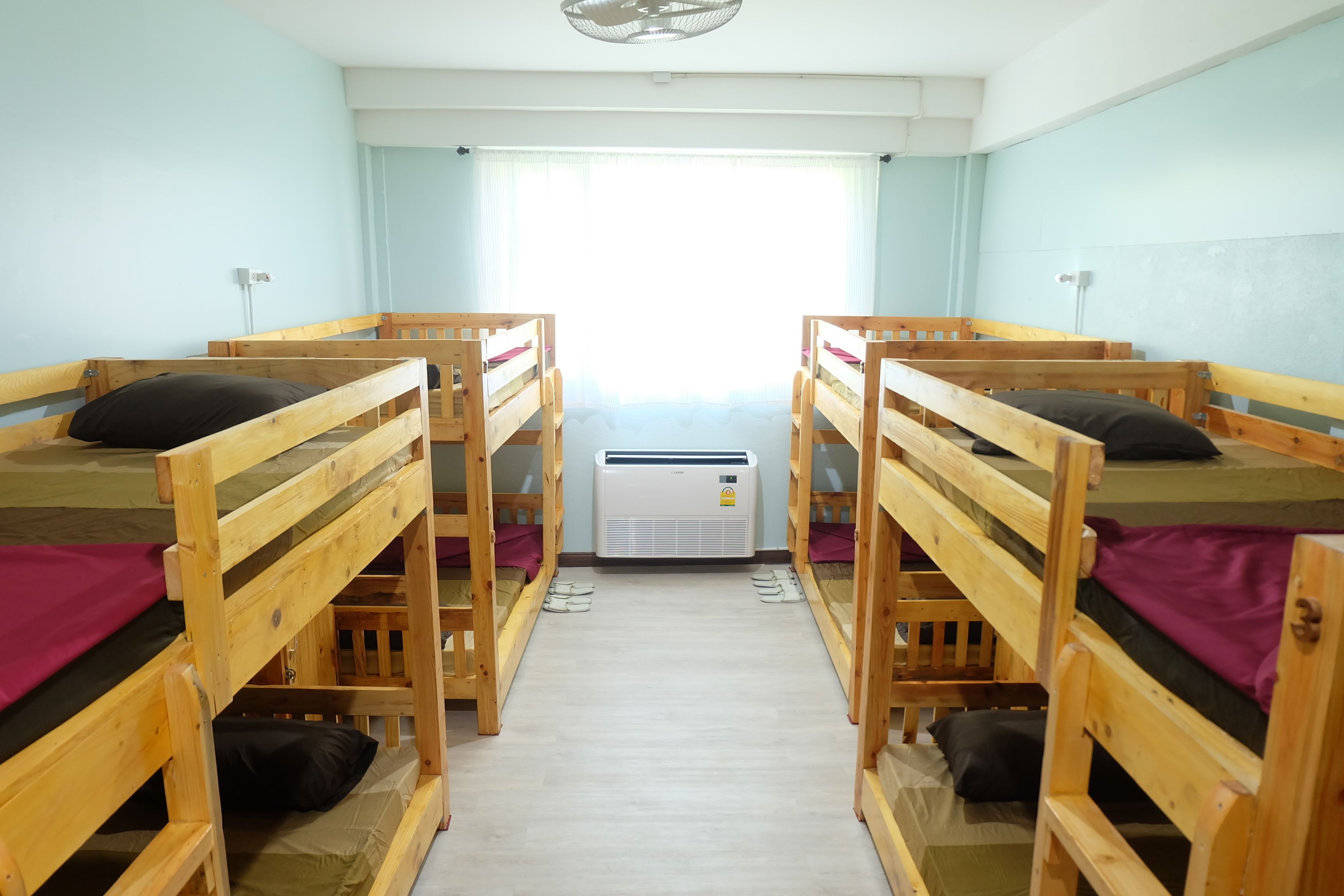 A dormitory room with four wooden bunk beds, each with a pillow and a blanket.