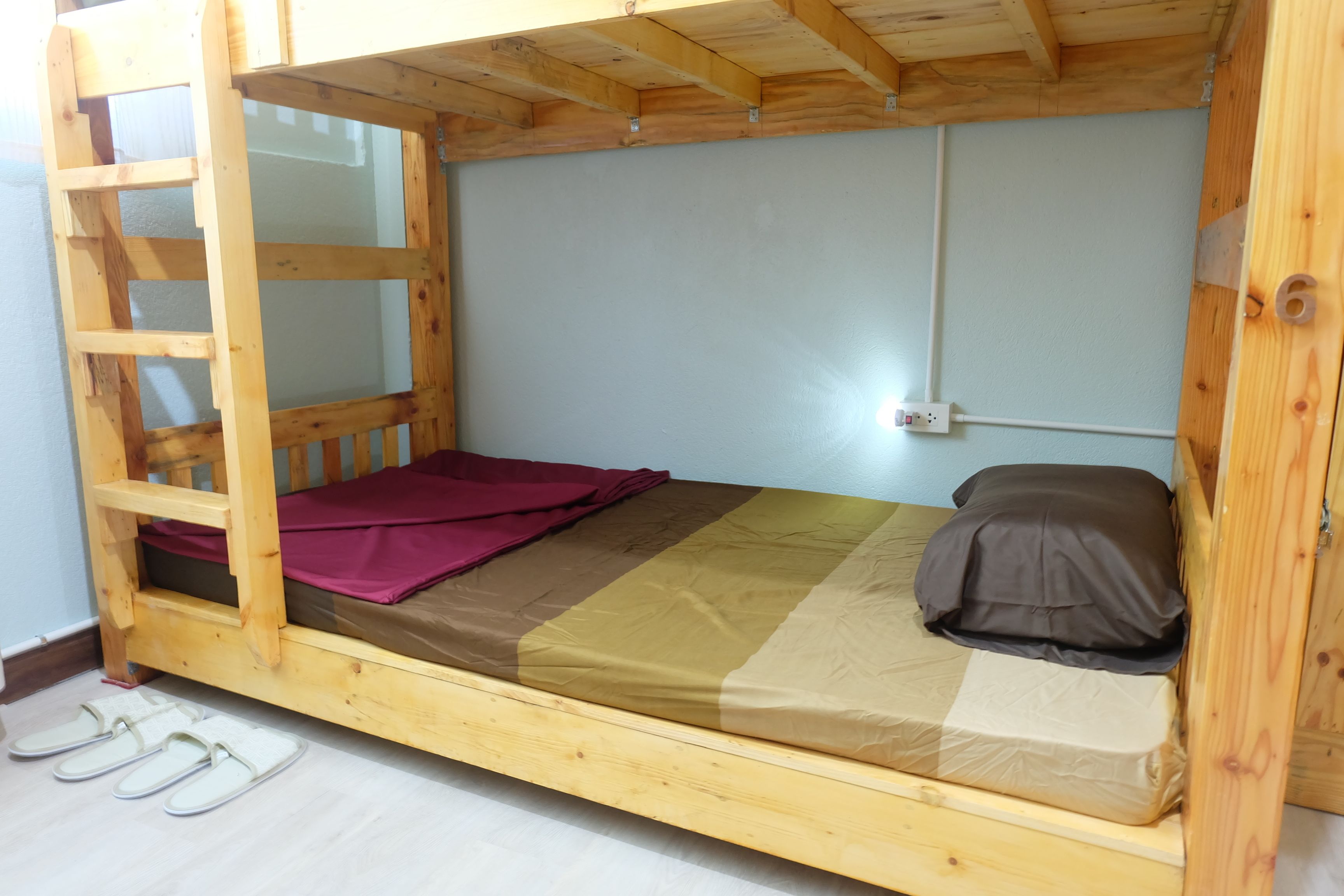 En säng med våningssäng i trä, med en stege, en madrass med ett brunt och beige täcke och en kudde.