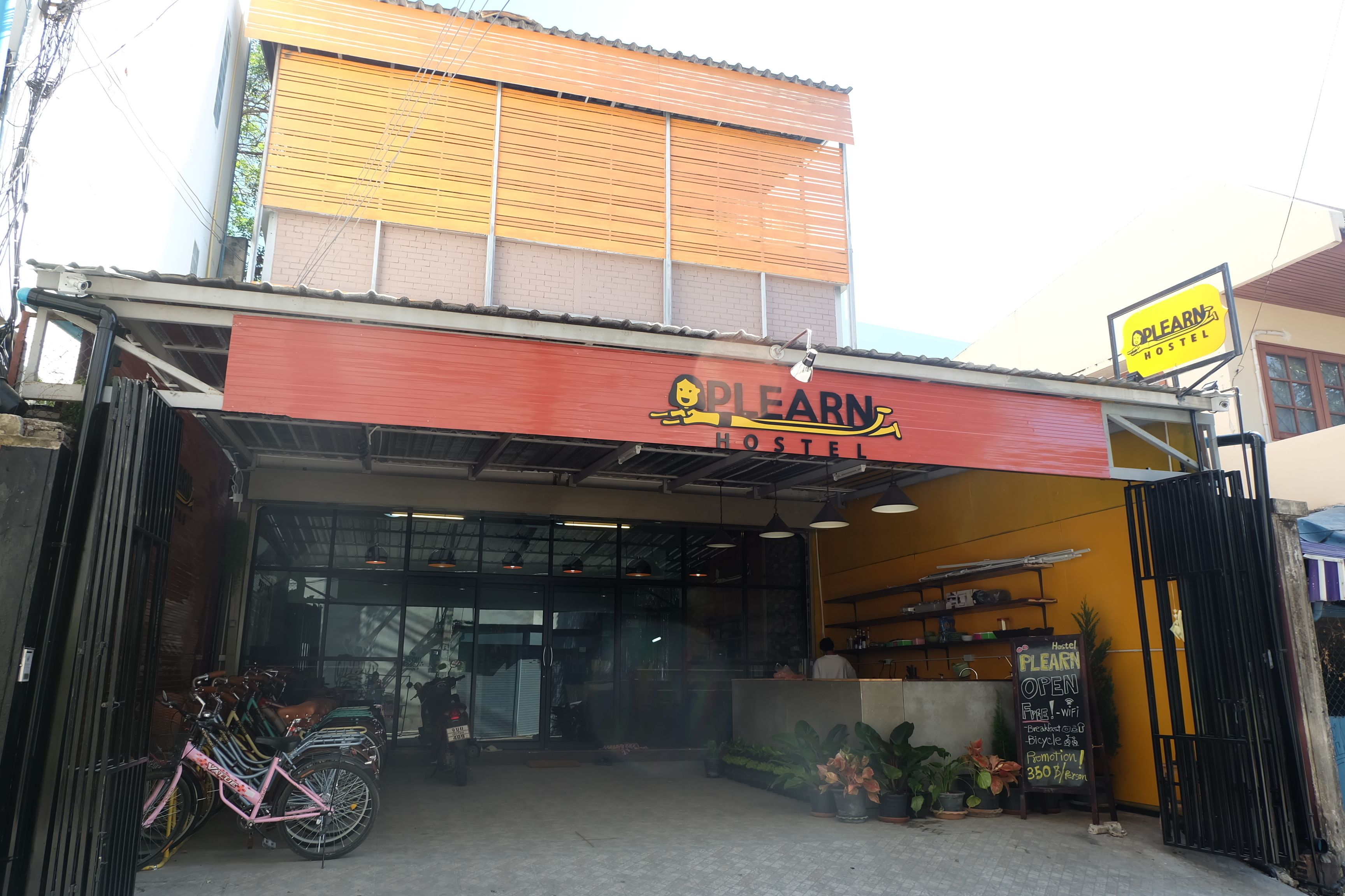 A hostel with a red and yellow facade, a sign indicating it's open, and bicycles parked outside.