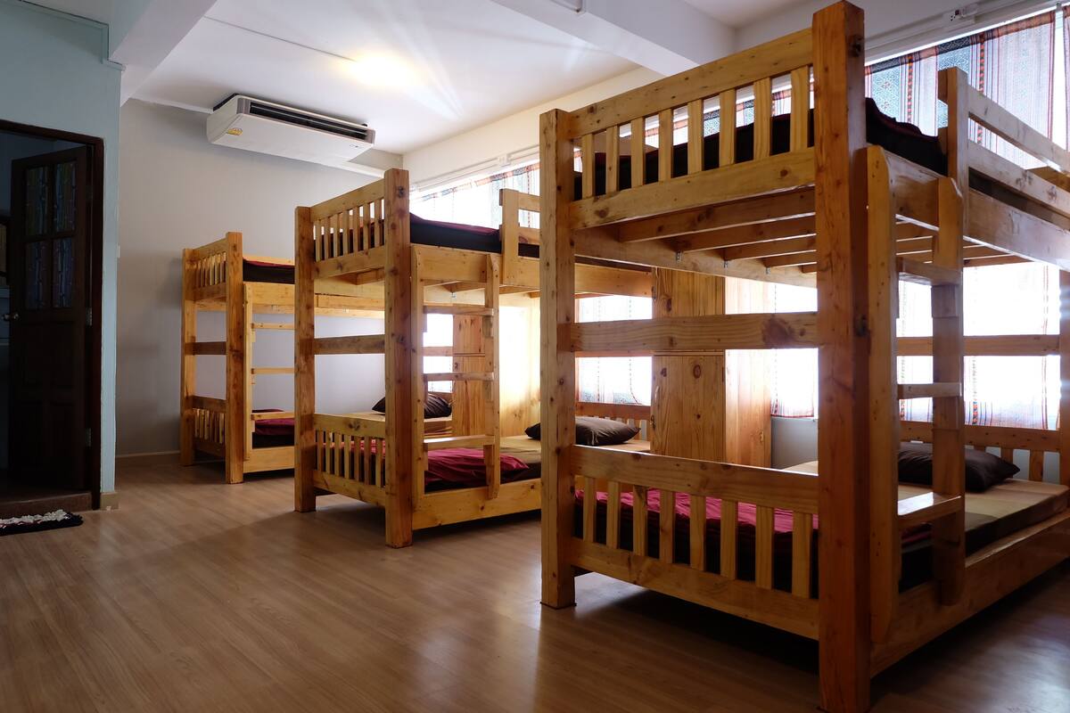 Bunk beds with wooden frames and slats, arranged in a row in a room with wooden flooring and white walls.