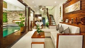 A modern living room with a pool, wooden flooring, and a staircase leading to an upper level. - Astagina Resort Villa And Spa (Legian)