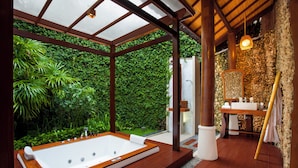 A modern bathroom with a large bathtub, a stone wall, and a wooden floor. - Astagina Resort Villa And Spa (Legian)