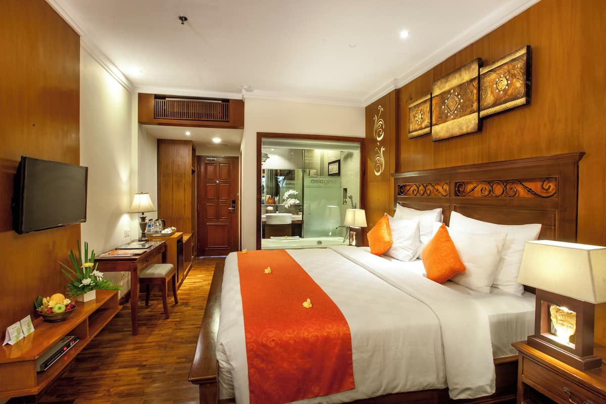 Hotelkamer met een groot bed, een televisie, een bureau met lamp en een badkamer zichtbaar door een geopende deur.