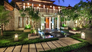 A traditional-style building with a water feature in front, surrounded by lush greenery and well-lit by ambient lighting. - Astagina Resort Villa And Spa (Legian)