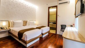A hotel room with a double bed, bedside tables, a small desk, a TV mounted on the wall, and an air conditioning unit. - Alimar Hotel (Malang)