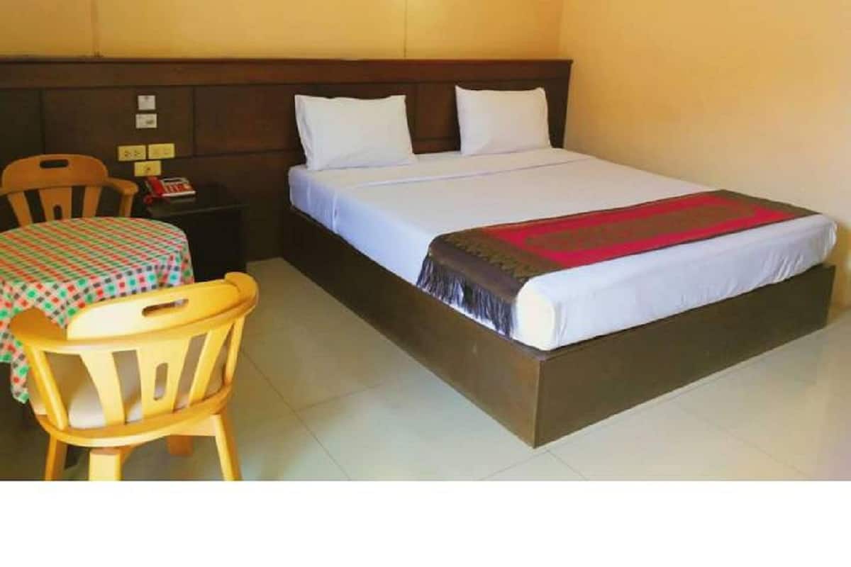 A single bed with a wooden headboard, a bedside table with a lamp, and a small table with a checkered tablecloth.