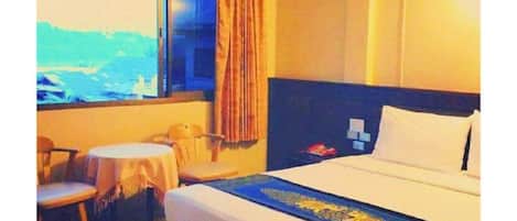 A hotel room with a bed, a desk, two chairs, a window with curtains, and a view of the outdoors.