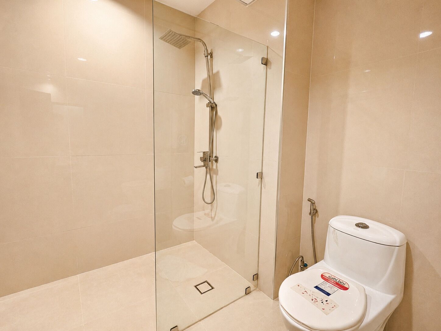 Un baño moderno con ducha cubierta de vidrio, inodoro blanco y paredes de azulejos color beige.