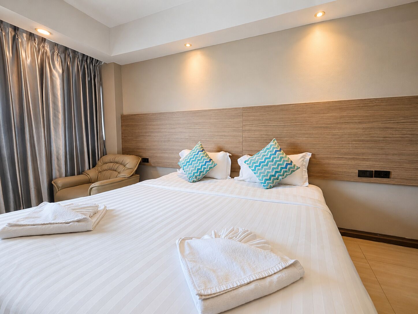 A hotel room with a large bed, a headboard, a chair, and a curtain.