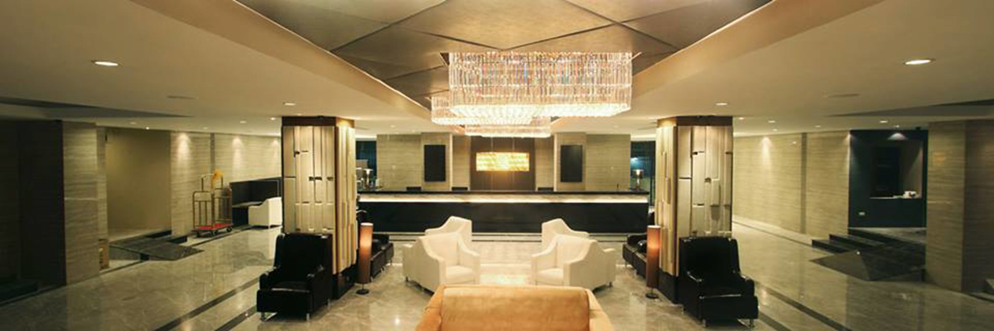 A spacious lobby with a central reception desk, multiple seating areas, and a large chandelier.