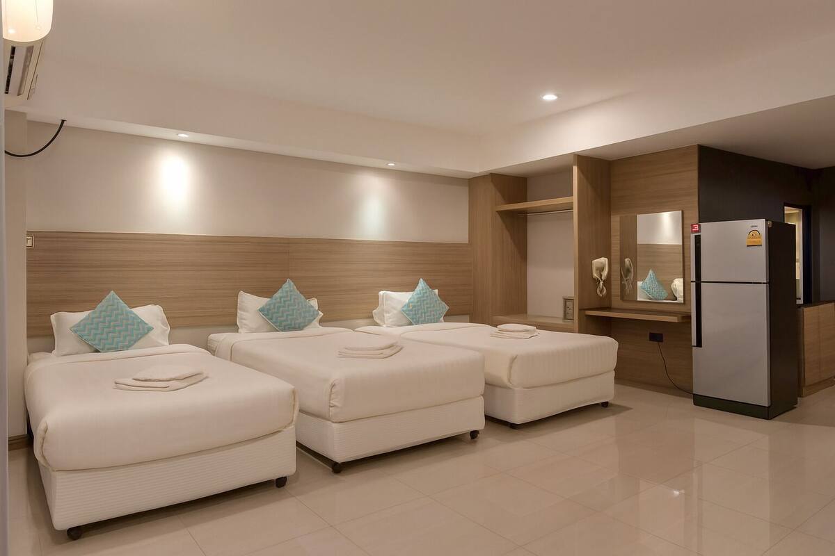 A hotel room with three beds, a minibar, a refrigerator, and a mirror.