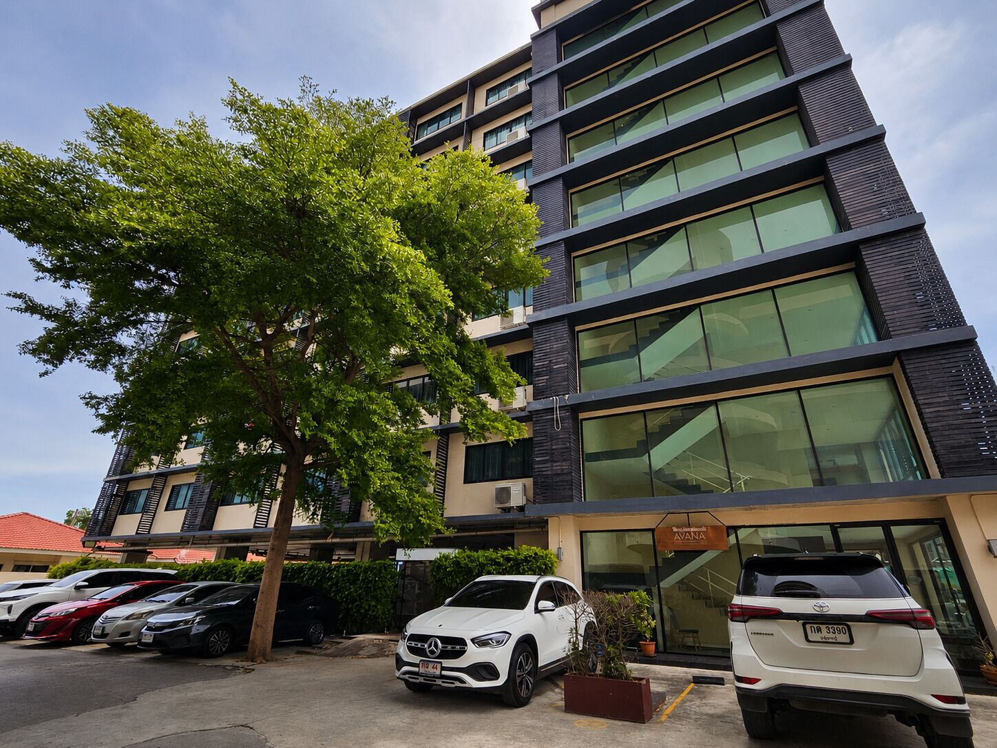 A multi-story building with a modern design, featuring large windows and a parking area with several cars.