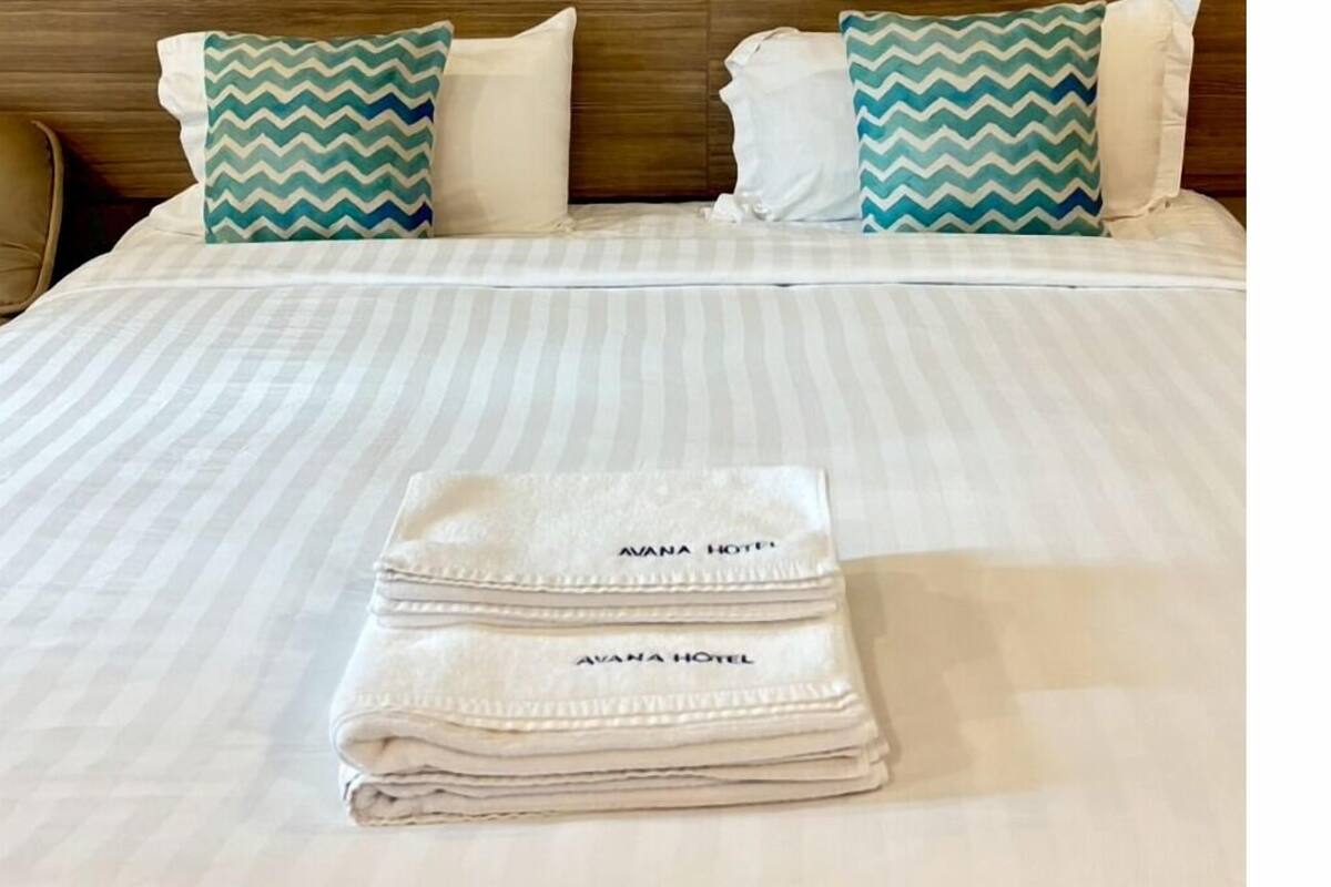 A neatly made bed with striped bedding, two pillows with a chevron pattern, and a folded towel with the hotel name on it.